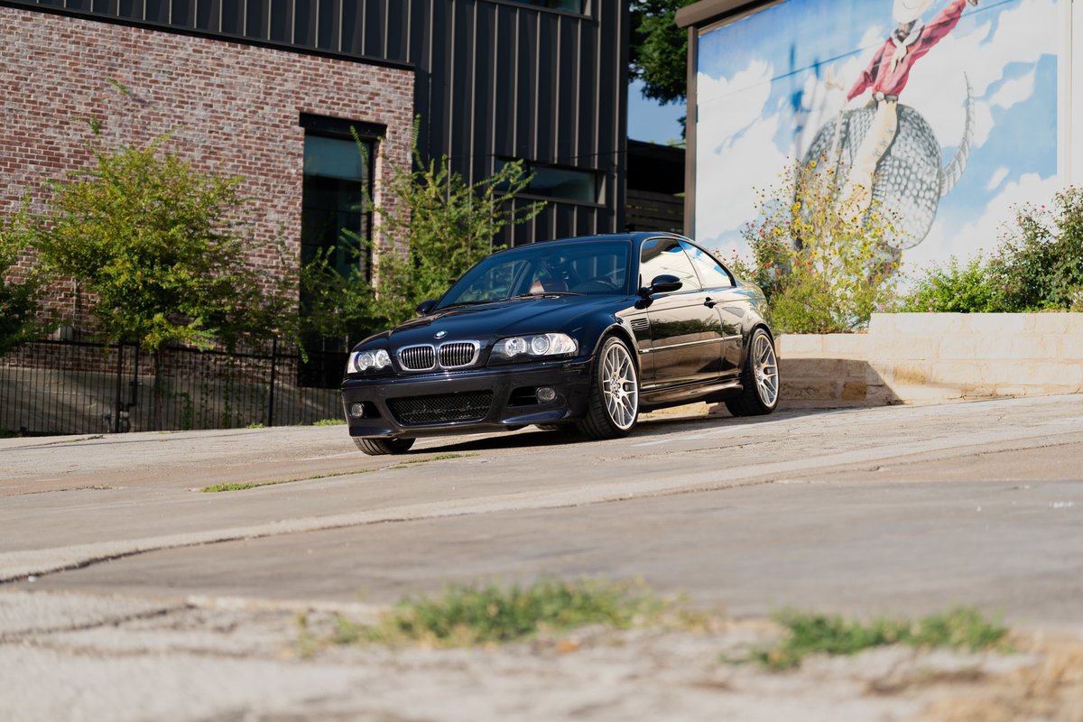 Black 2002 BMW M3 with silver alloy rims parked near a mural.