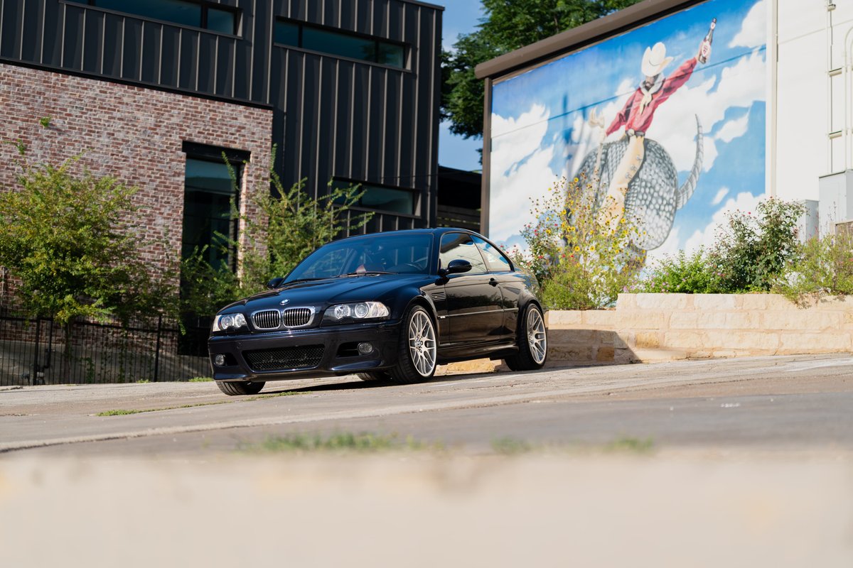 Black 2002 BMW M3 Coupe with silver alloy rims parked in front of a mural.