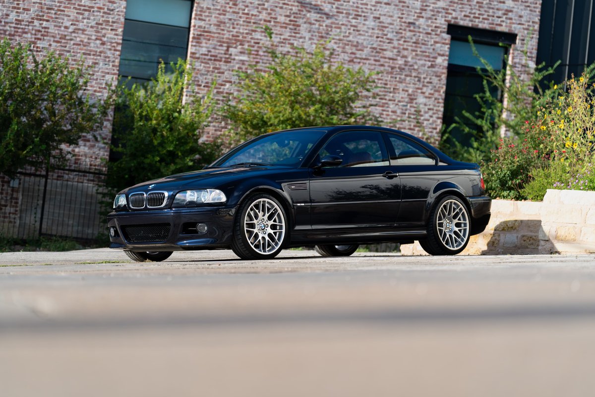 A black 2002 BMW M3 coupe with silver multispoke rims parked outdoors.