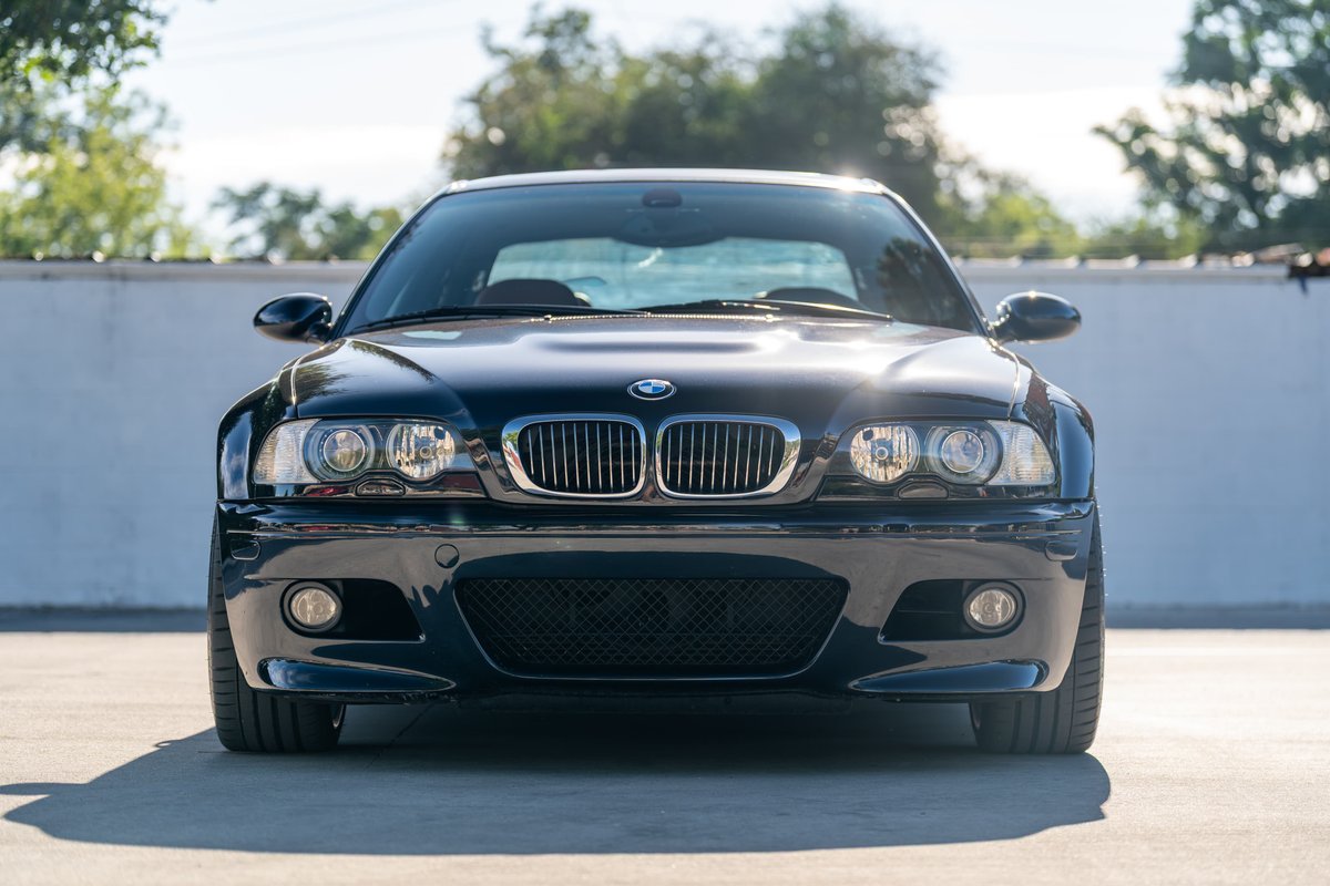 Front view of a carbon black 2002 BMW M3 with chrome grille and clear headlights.