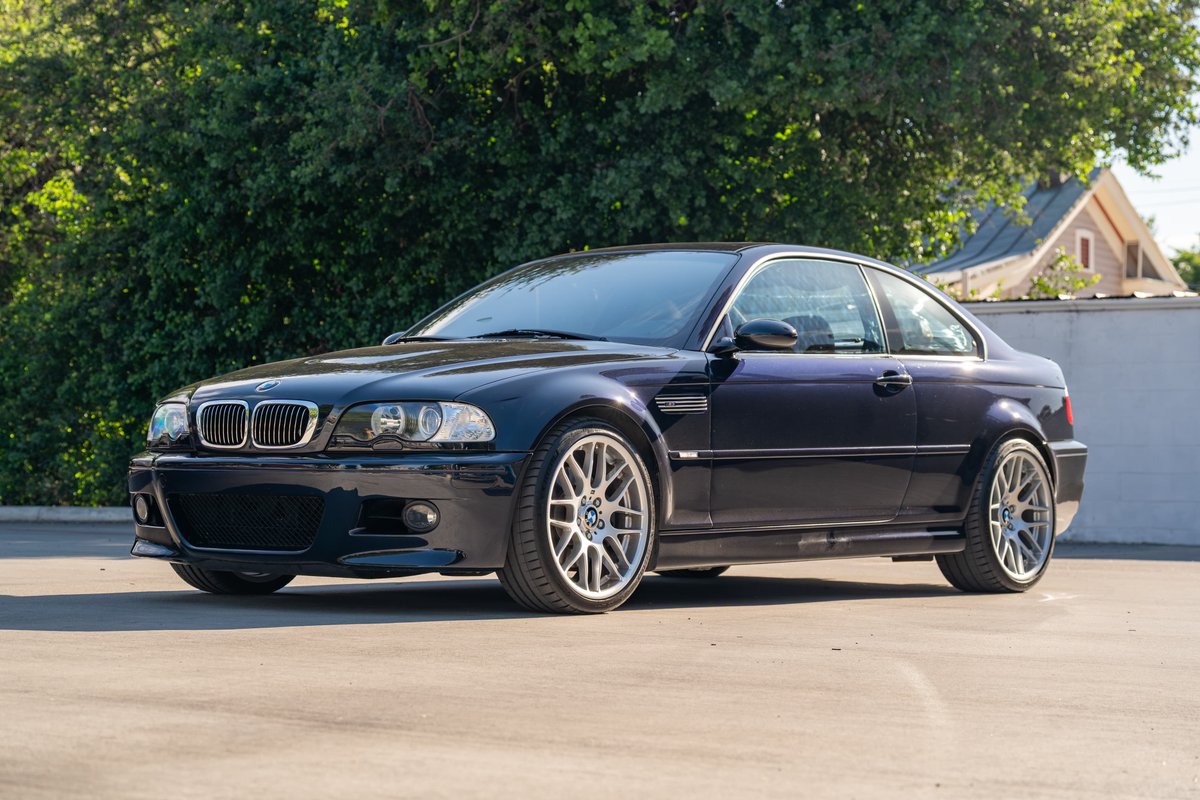 A dark blue 2002 BMW M3 coupe with silver multi-spoke rims is parked on asphalt.