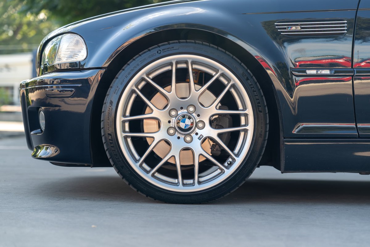 Close up of the front wheel of a carbon black 2002 BMW M3 with its iconic M Sport rims.