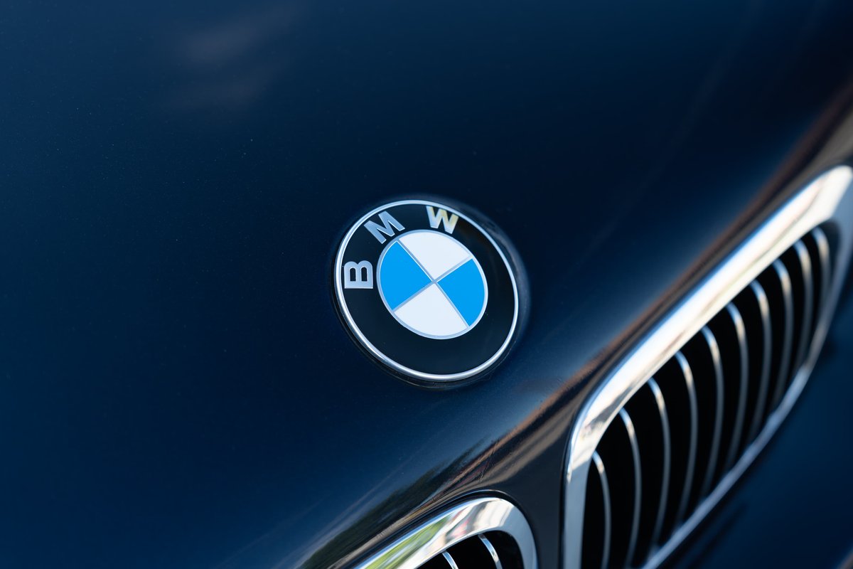Close up of the BMW emblem on a carbon black 2002 BMW M3 hood, with chrome grille trim.