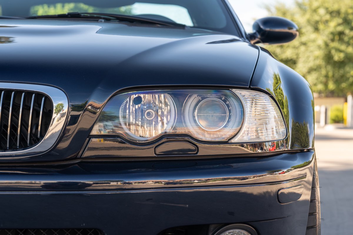 Closeup of the front headlight and chrome grille of a black 2002 BMW M3.
