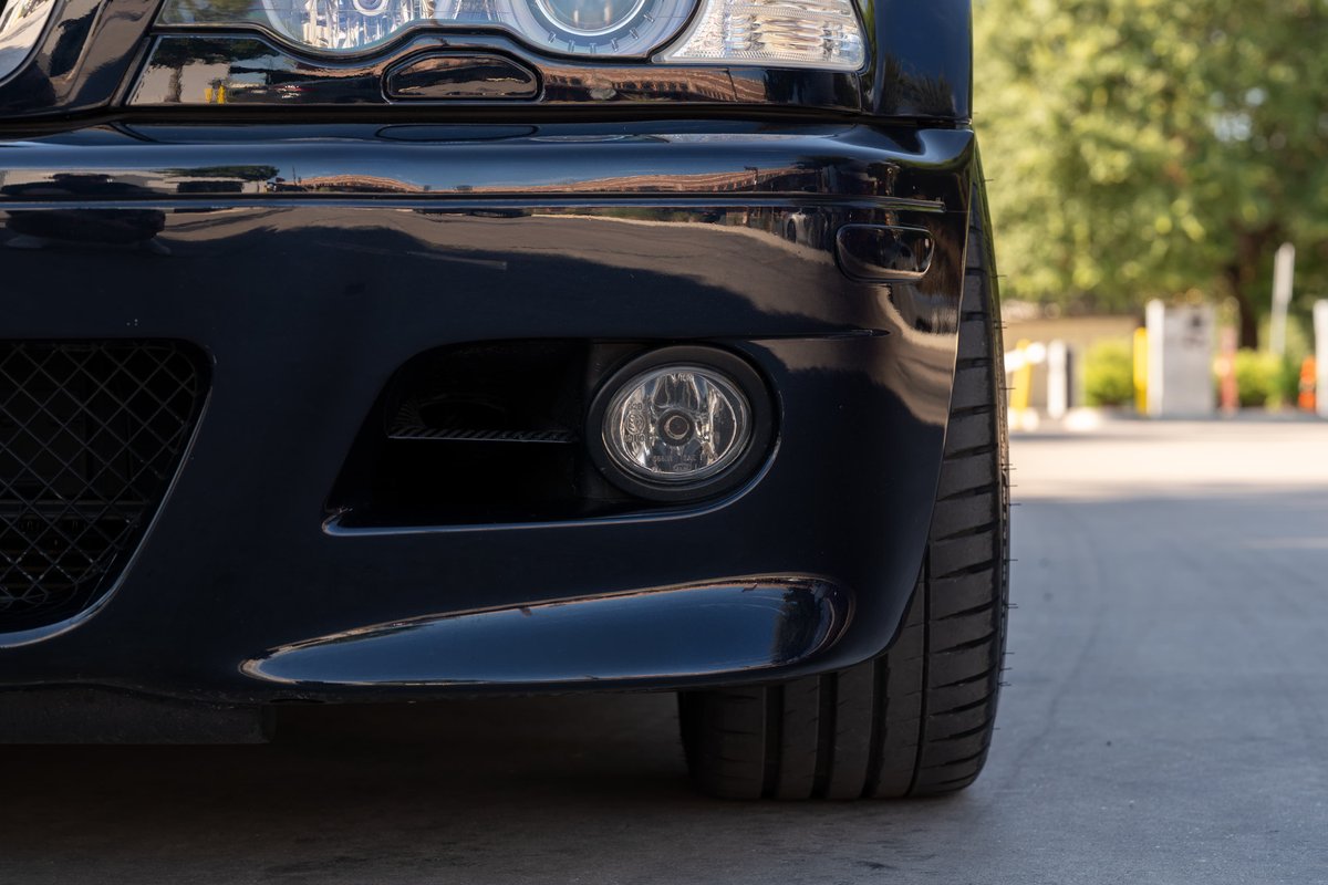 Close-up of a carbon black 2002 BMW M3's front bumper and tire.