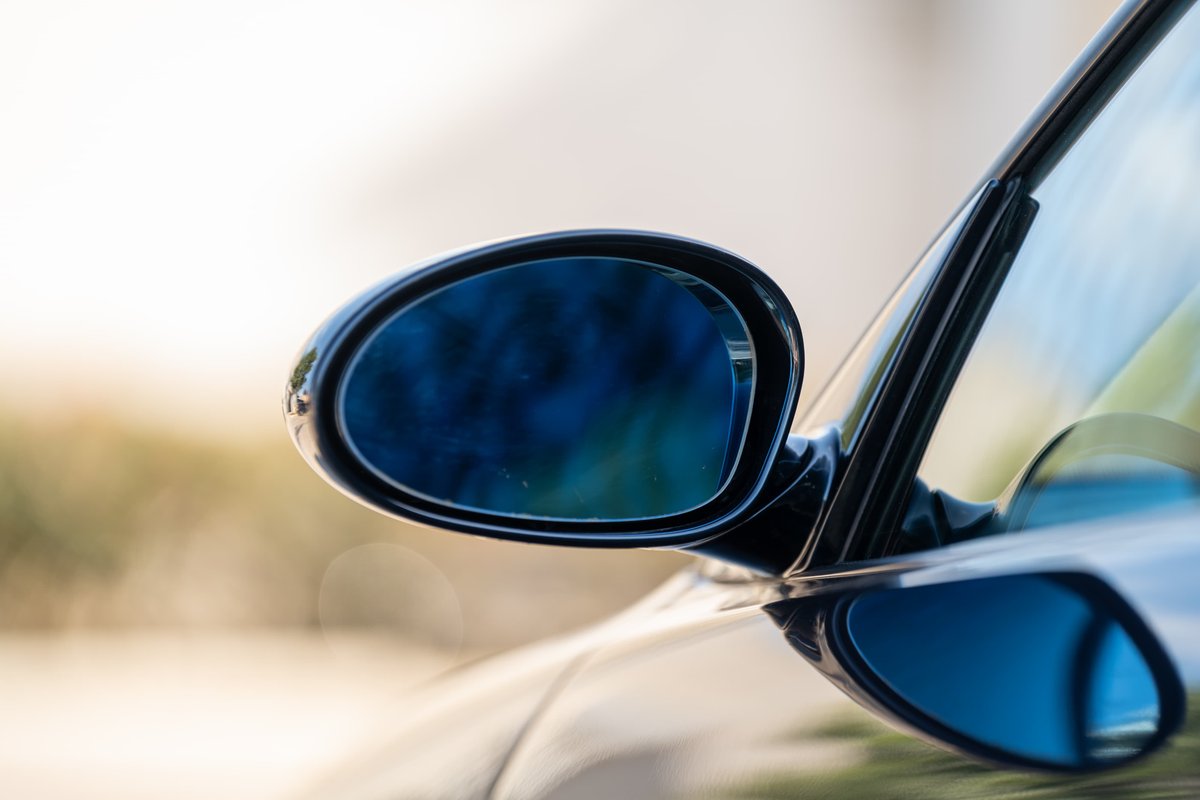 Close-up of a blue-tinted side mirror and part of the windshield trim on a black 2002 BMW M3.