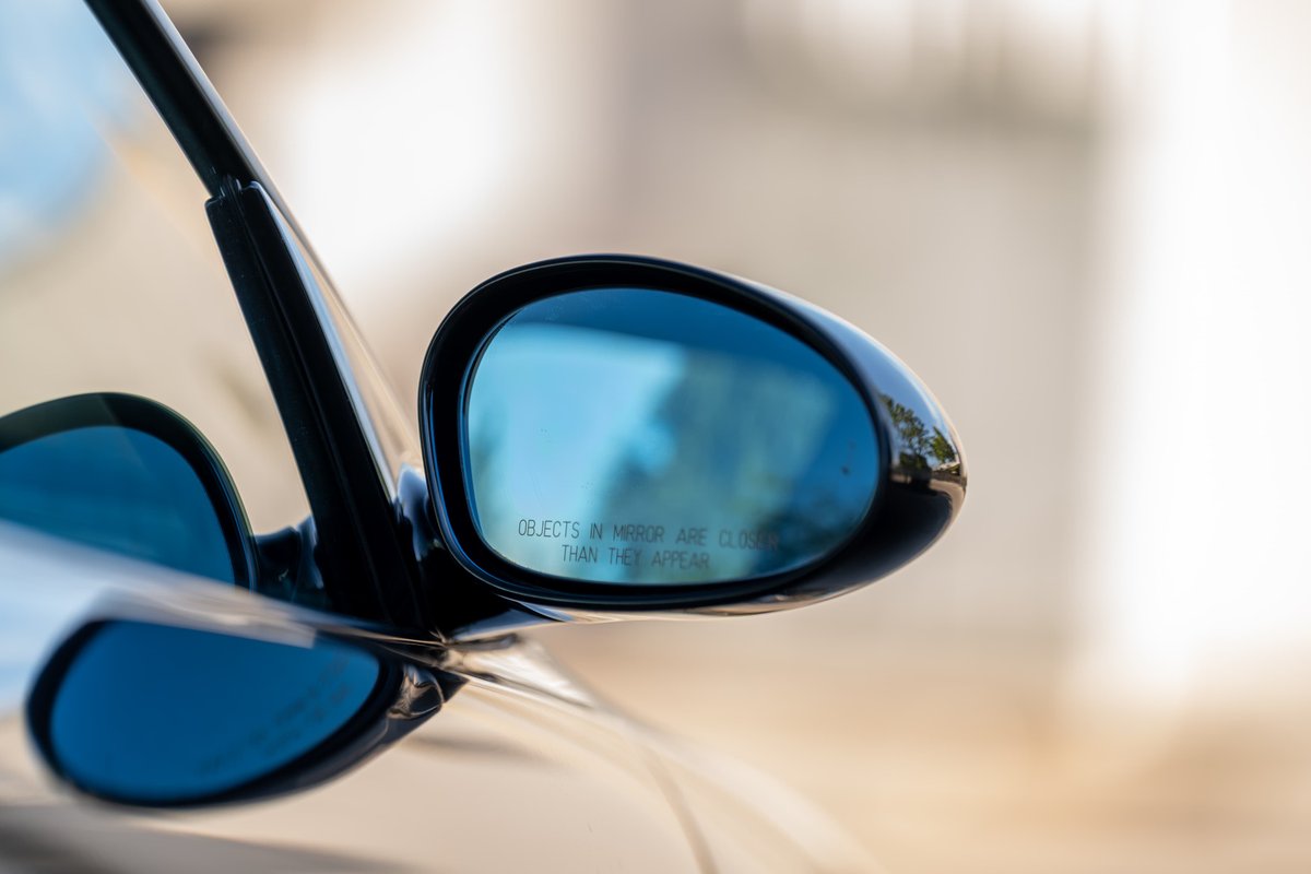Close-up of a black 2002 BMW M3's side mirror with blue tint.