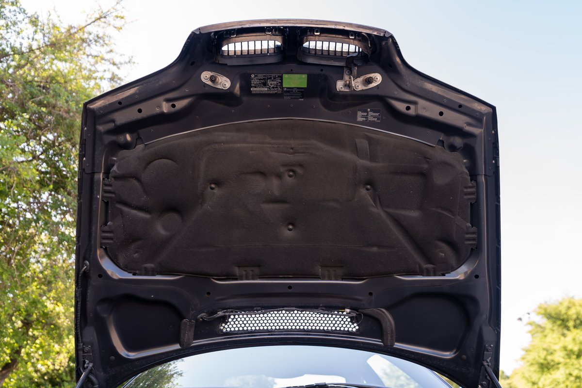 Under the hood of a carbon black 2002 BMW M3. Hood insulation and vents visible.
