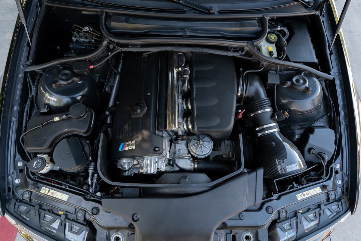BMW M3 engine bay with carbon fiber intake and M tri-color badge.