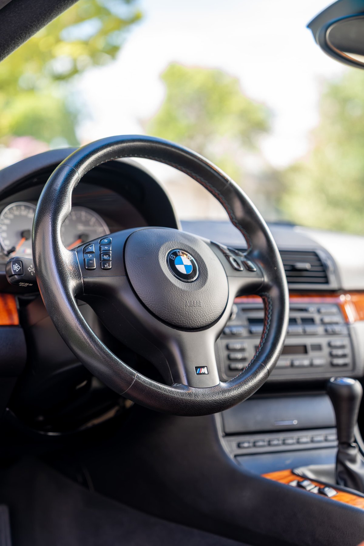 Carbon black 2002 BMW M3 steering wheel with M badge and wood trim.