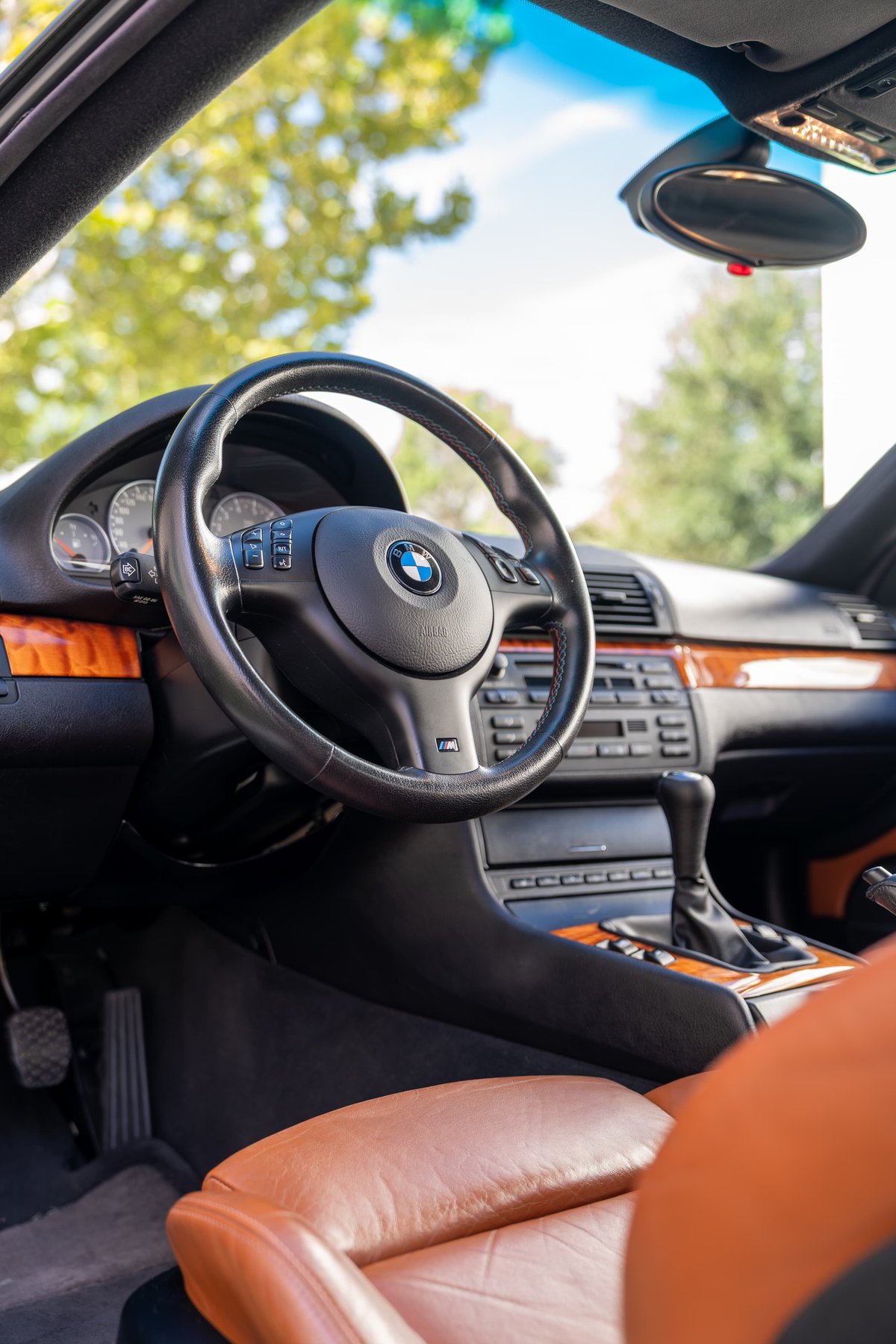 Interior view of a Carbon Black 2002 BMW M3 convertible with wood trim and tan leather seats.