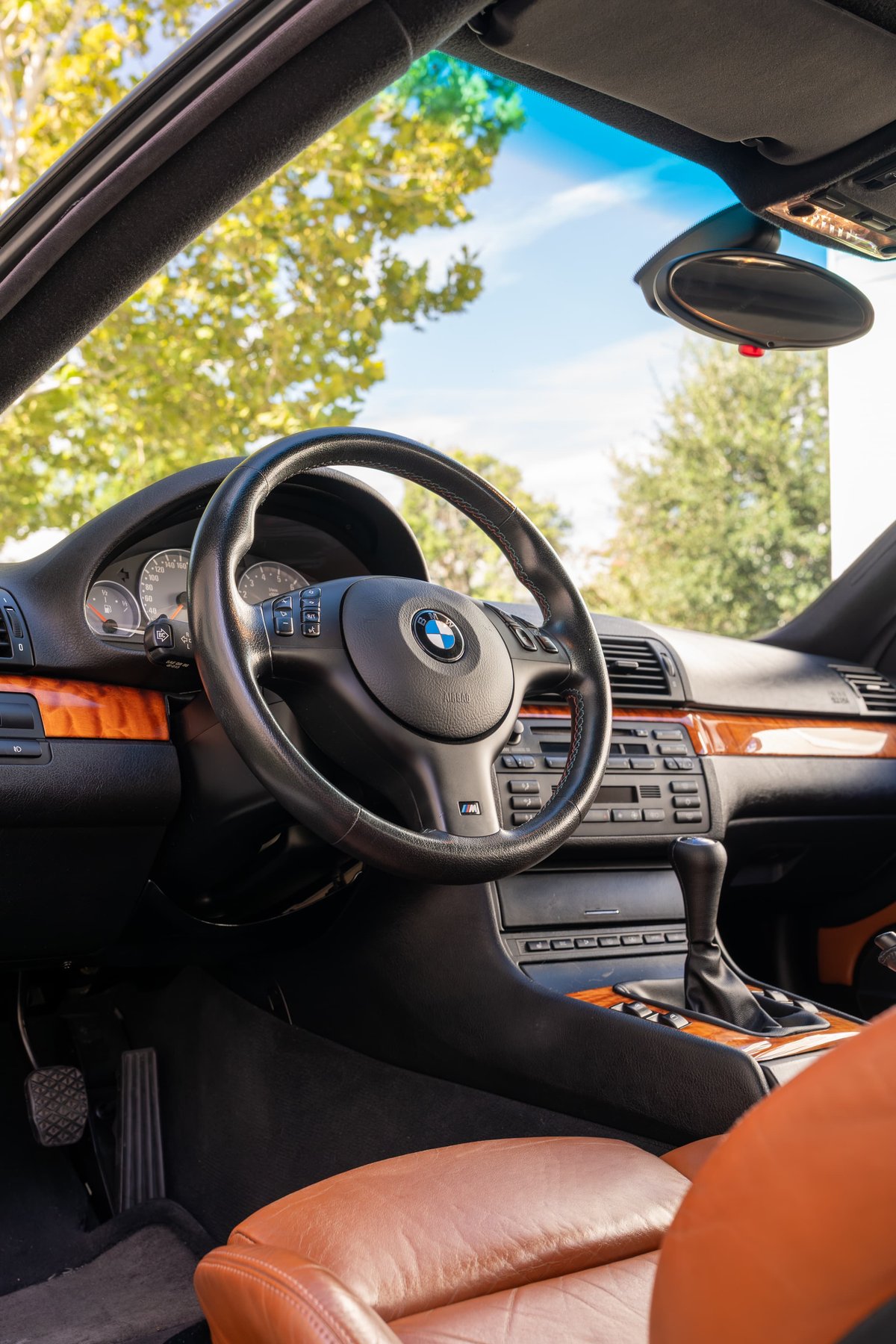 Interior view of a black 2002 BMW M3 convertible with wood trim and tan leather seats.
