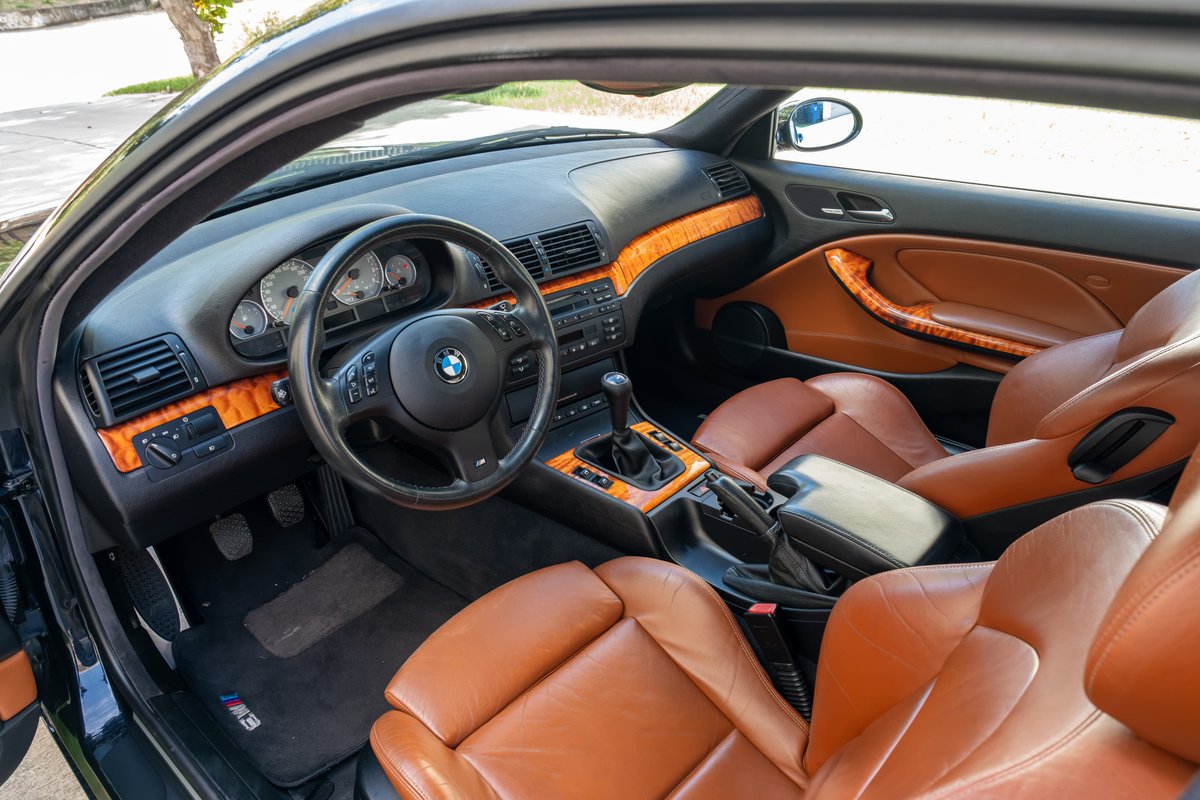 Black 2002 BMW M3 interior with tan leather seats and wood trim.
