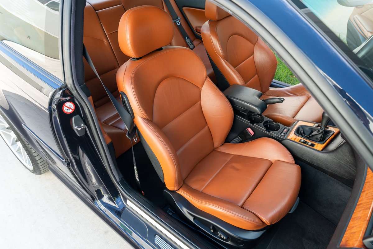 Carbon black 2002 BMW M3 coupe with tan leather sport seats and wood trim interior.