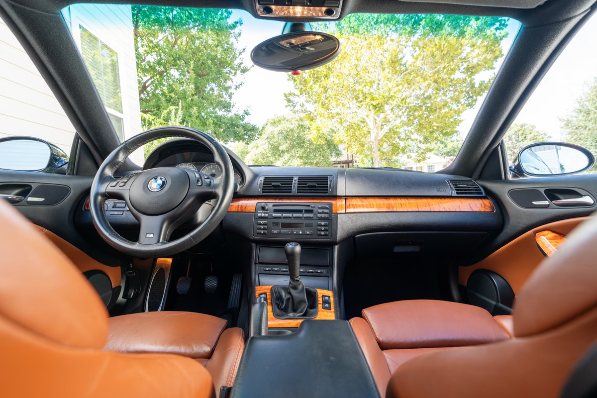 BMW M3 interior with orange leather seats, wood trim, and manual shifter.