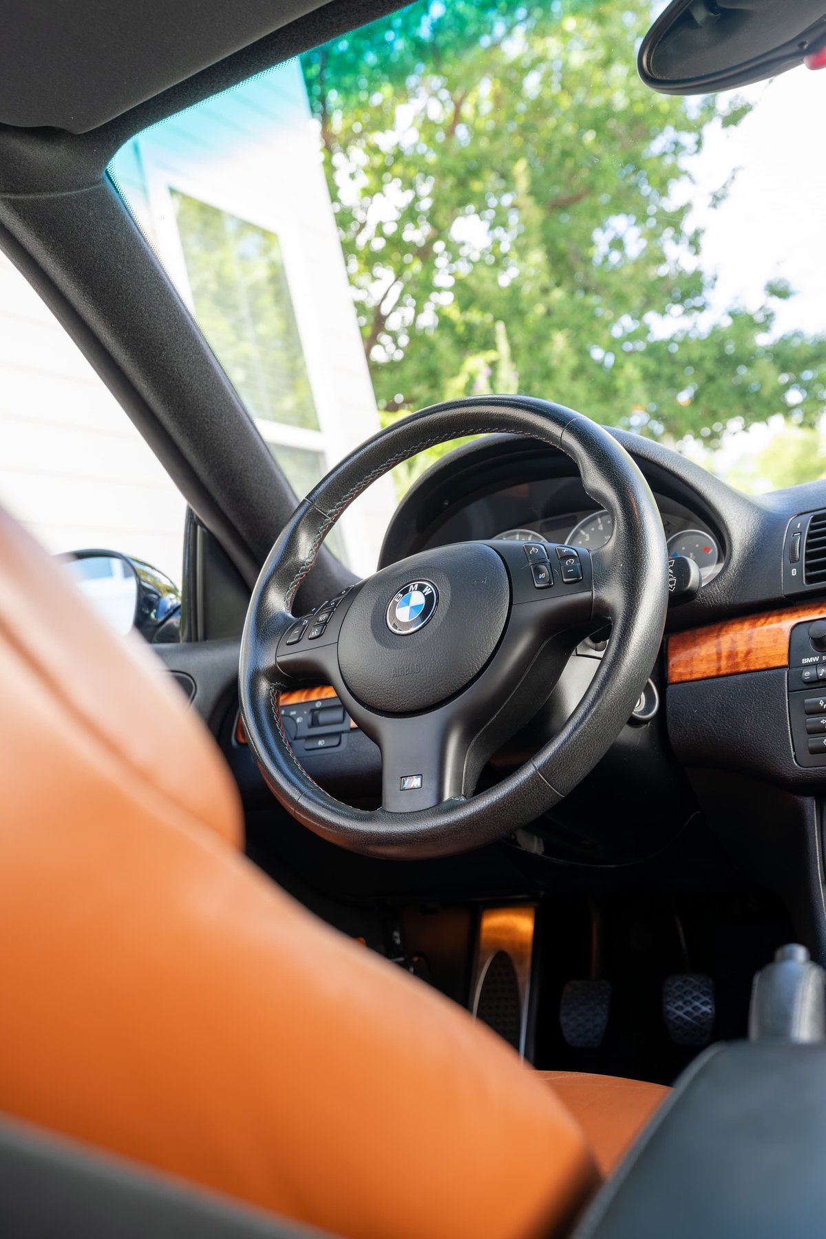 Interior view of a 2002 BMW M3 in Carbon Black, featuring tan leather seats and wood trim.