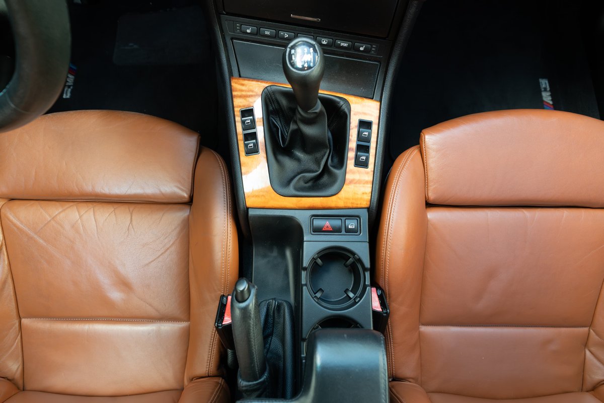 2002 BMW M3 interior with tan leather seats, wood trim, and 6-speed manual shifter.