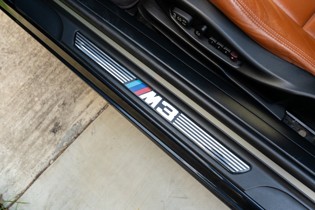 Black 2002 BMW M3 door sill trim with M stripes and tan leather seat.