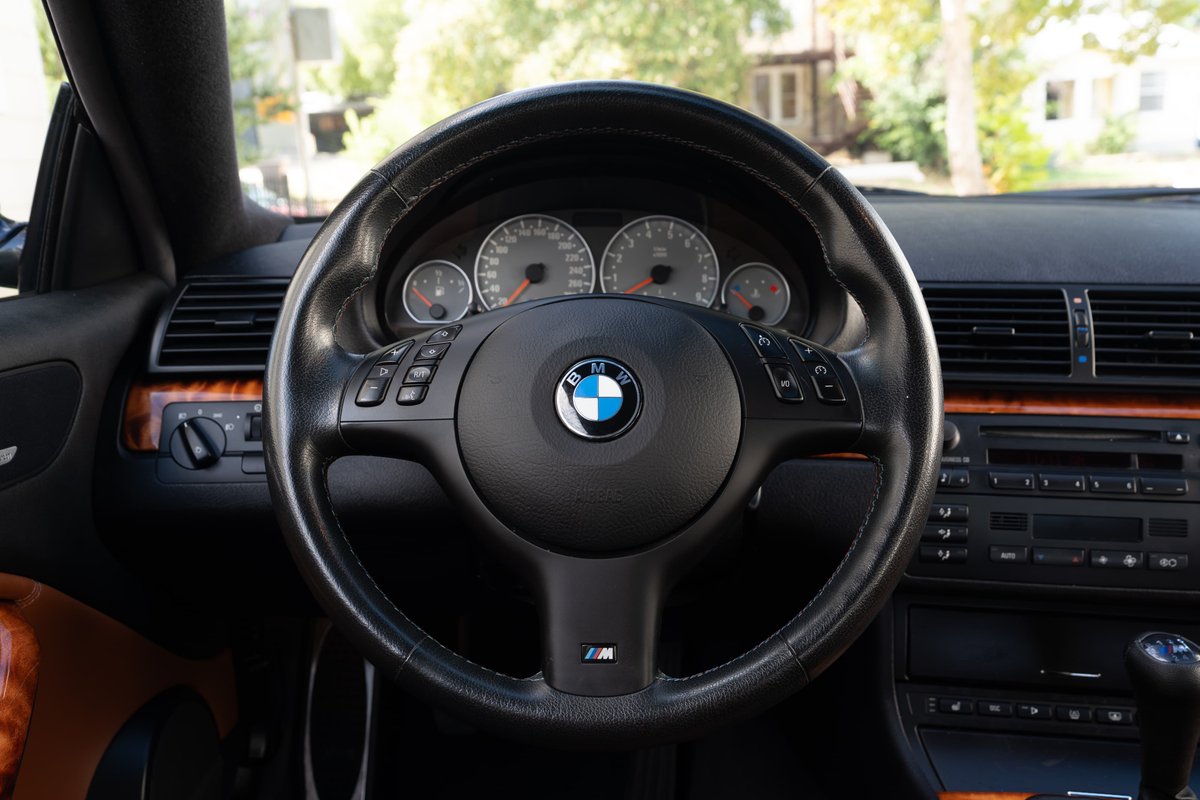 2002 BMW M3 steering wheel and dashboard with carbon black interior trim.