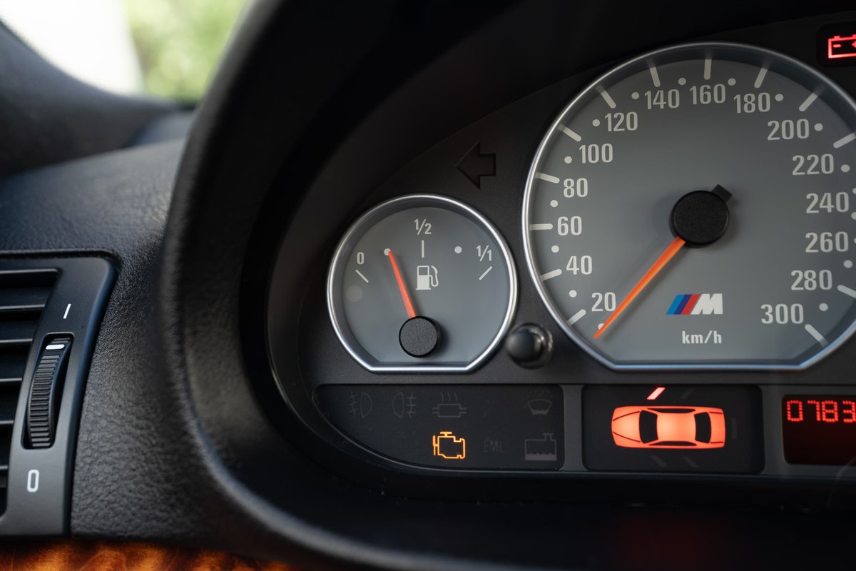 Close-up of a 2002 BMW M3 dashboard, showing the speedometer, fuel gauge, and illuminated car warning light.