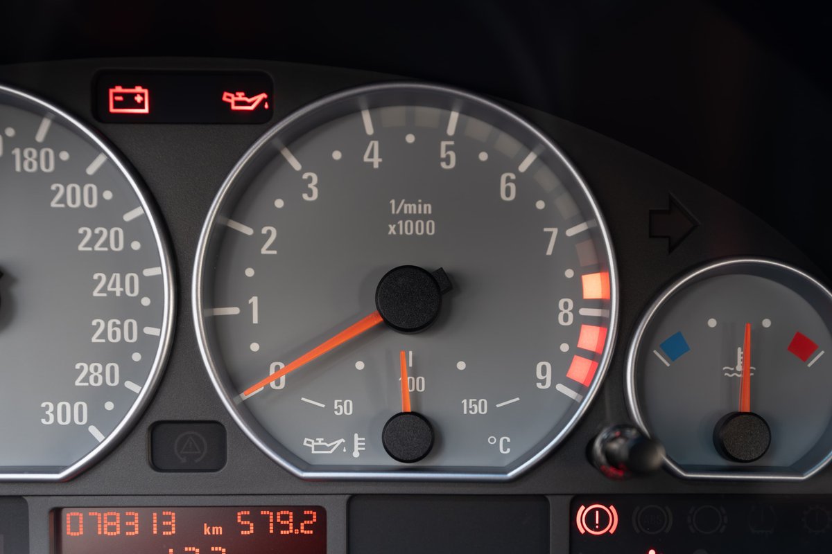 Dashboard gauges in a black 2002 BMW M3, showing tachometer, speedometer, oil temp, and battery warning.