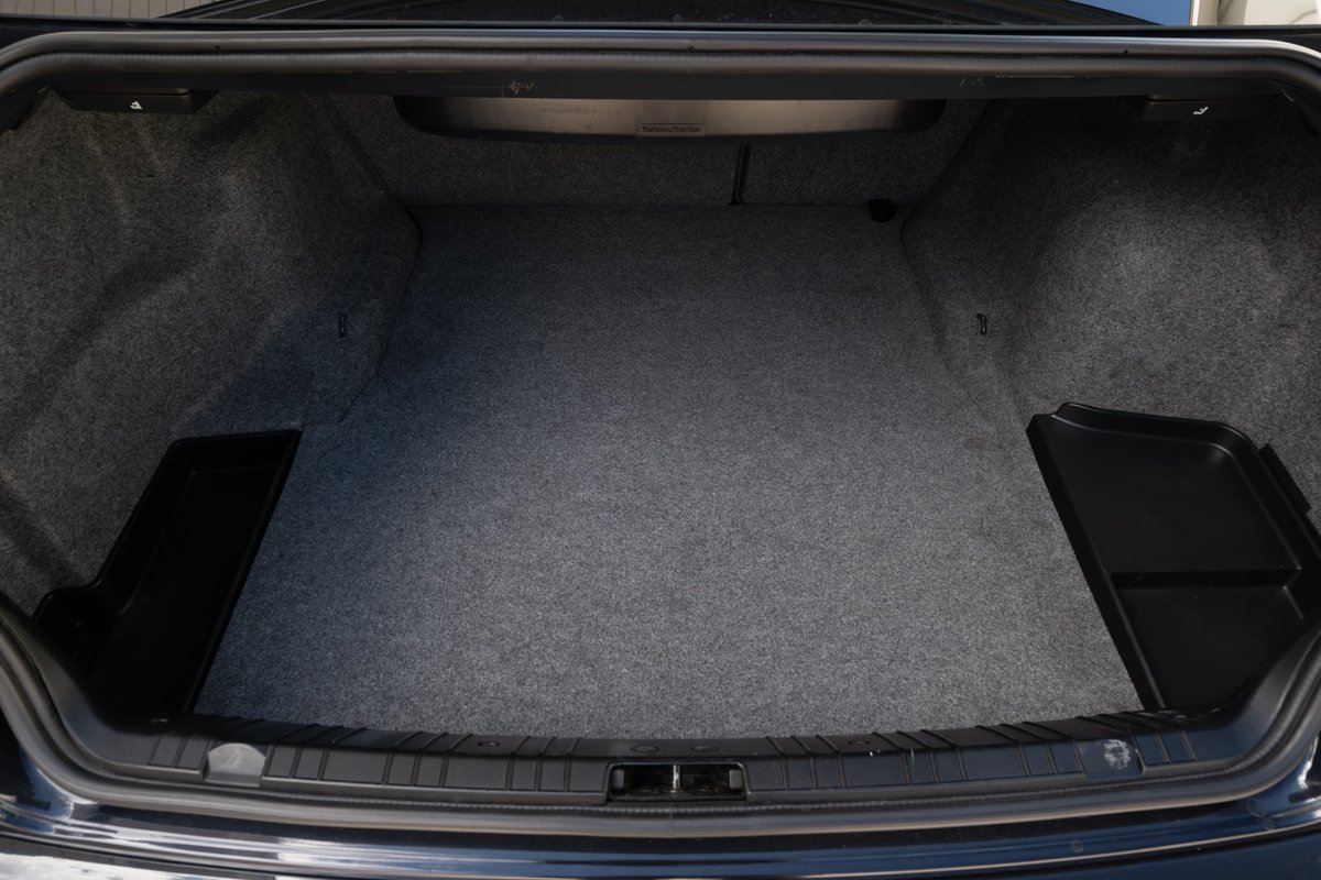 Interior shot of the trunk of a Carbon Black 2002 BMW M3, featuring grey carpeting and black trim.
