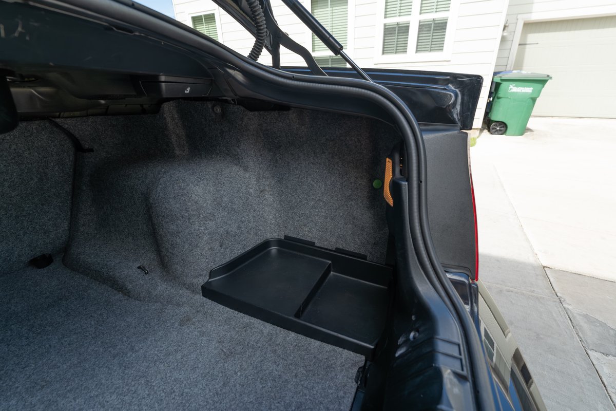 Trunk of a black 2002 BMW M3 with carpeted interior and a removable tray.