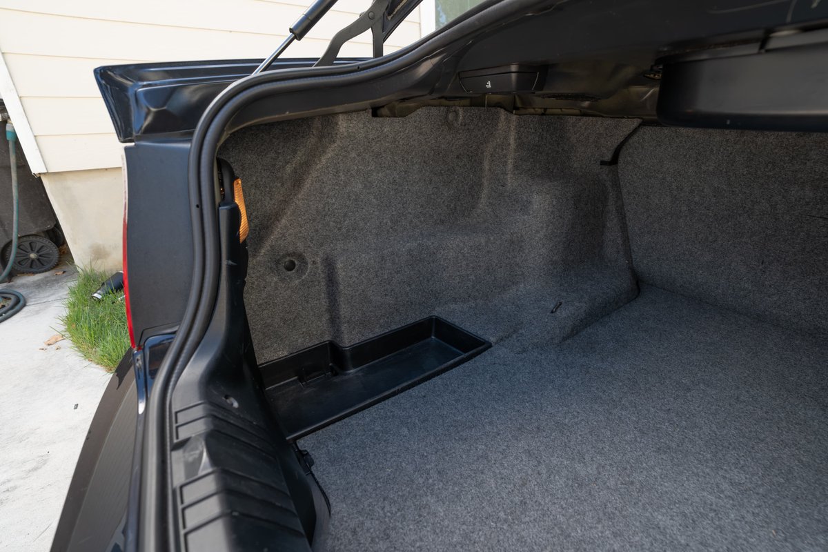 Black 2002 BMW M3 trunk, carpeted with plastic storage tray.