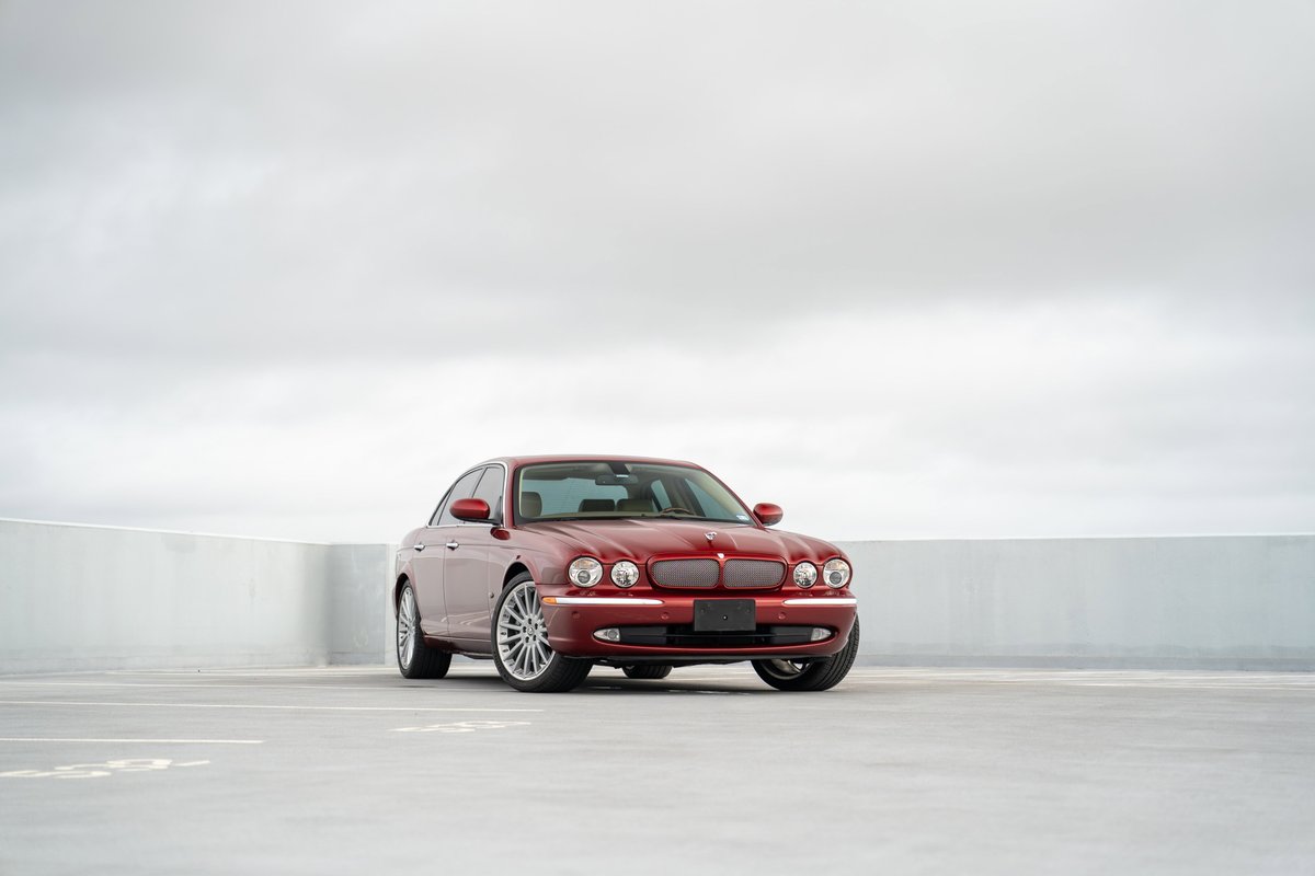 A red 2006 Jaguar XJR sedan with chrome rims and trim sits on a concrete surface.