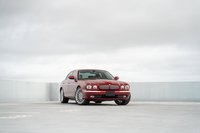 A red 2006 Jaguar XJR sedan with chrome rims and trim sits on a concrete surface.