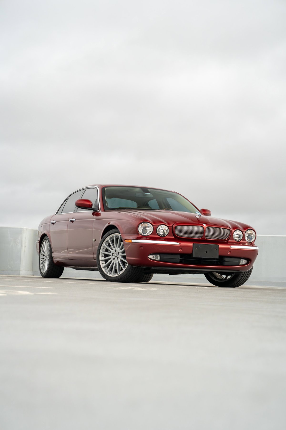 A red 2006 Jaguar XJR sedan with silver multi-spoke rims and chrome trim.
