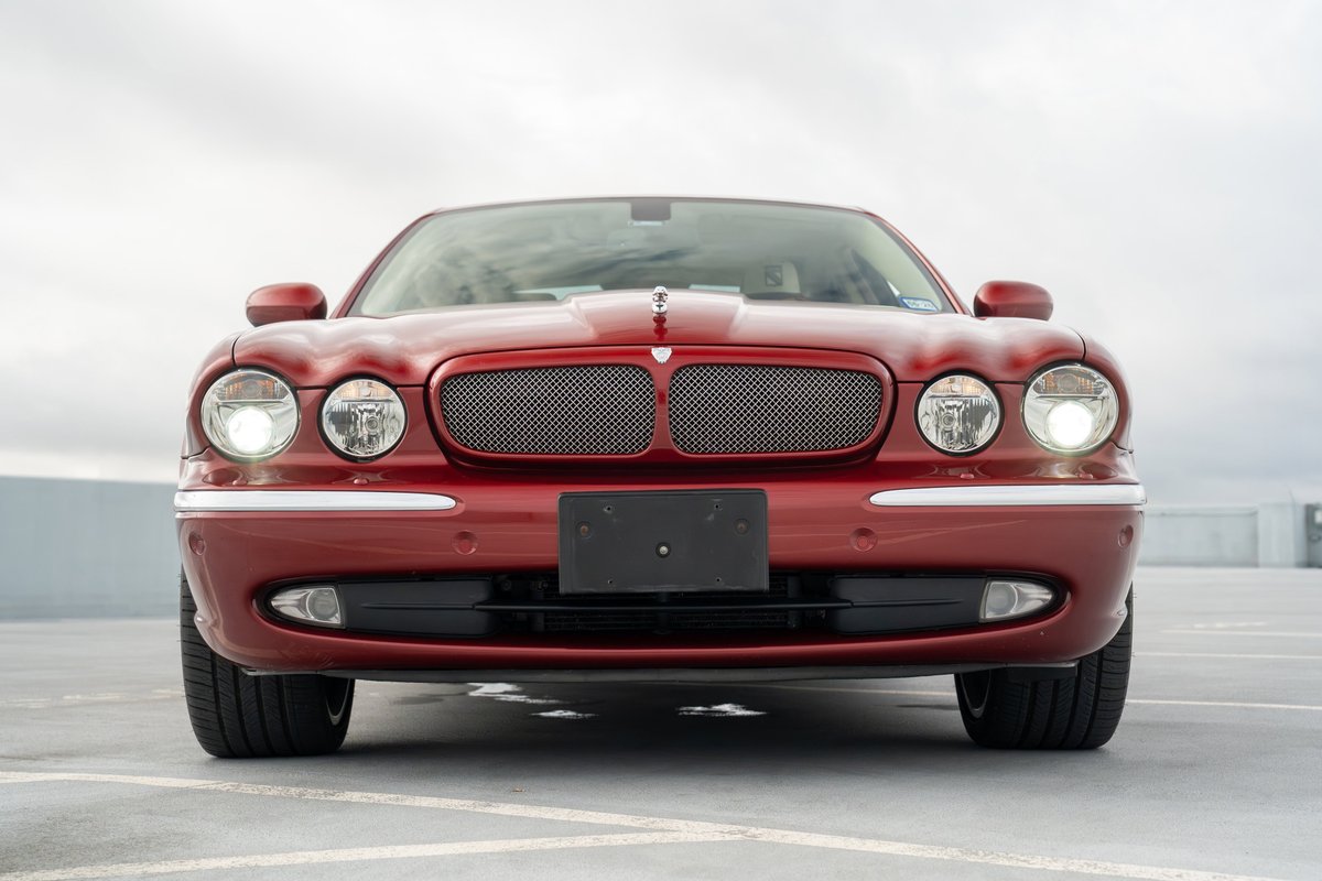 Front view of a red 2006 Jaguar XJR sedan, featuring chrome trim, a mesh grille, and dual headlights.