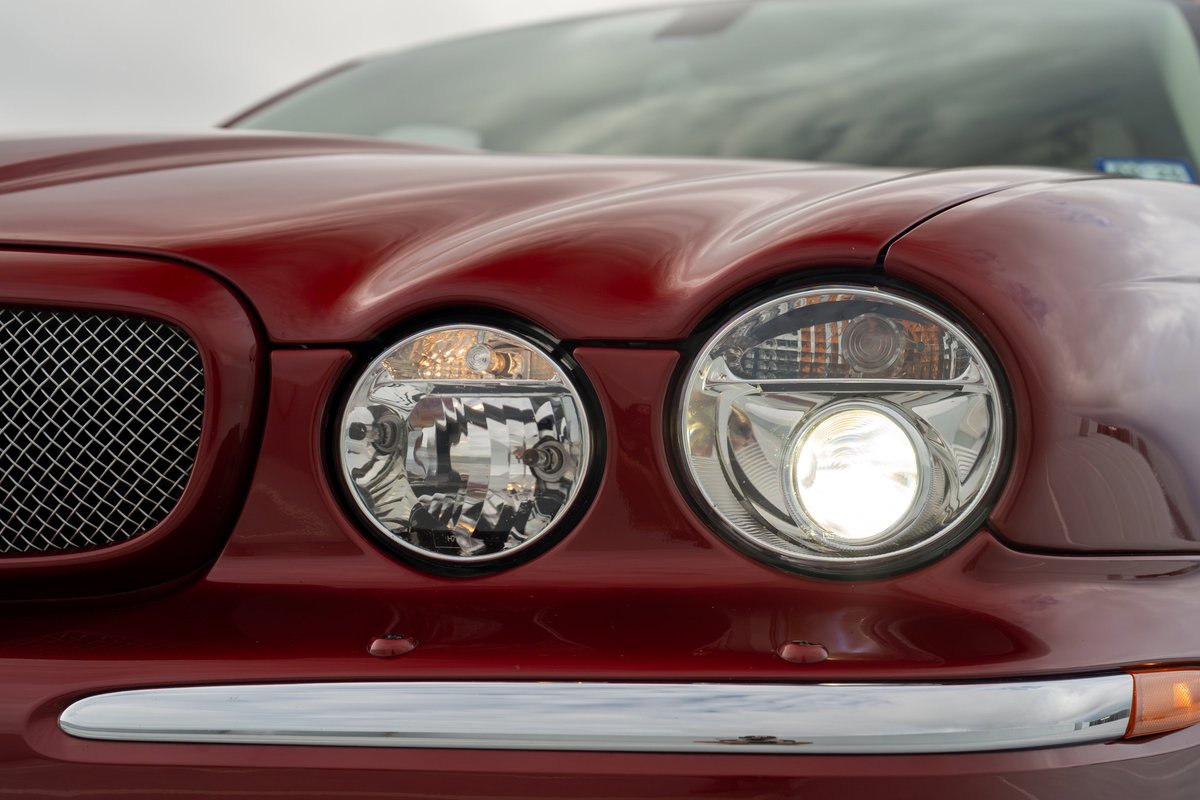 Close-up of a red 2006 Jaguar XJR's dual round headlights and chrome grille.