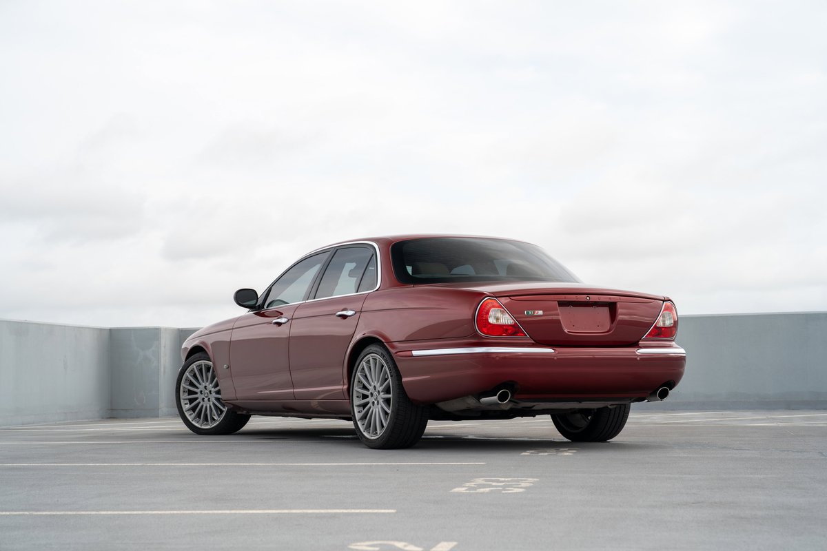Rear view of a ruby red 2006 Jaguar XJR sedan with multi-spoke alloy rims.