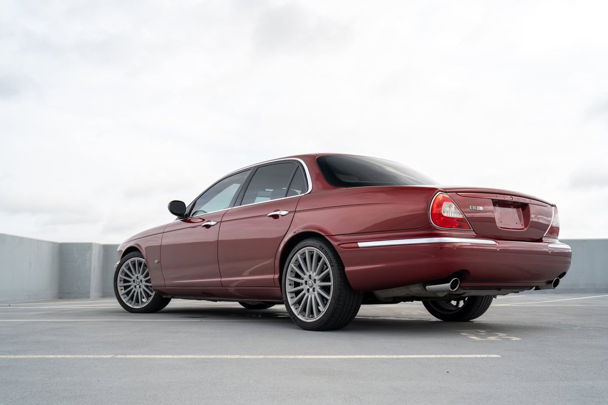 Rear 3/4 view of a red 2006 Jaguar XJR sedan, with chrome trim and silver alloy rims.