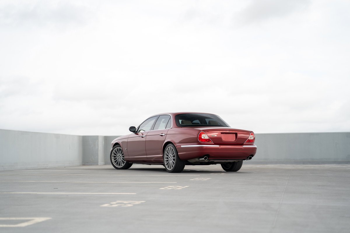 Rear view of a red 2006 Jaguar XJR sedan with multi-spoke alloy rims parked outdoors.