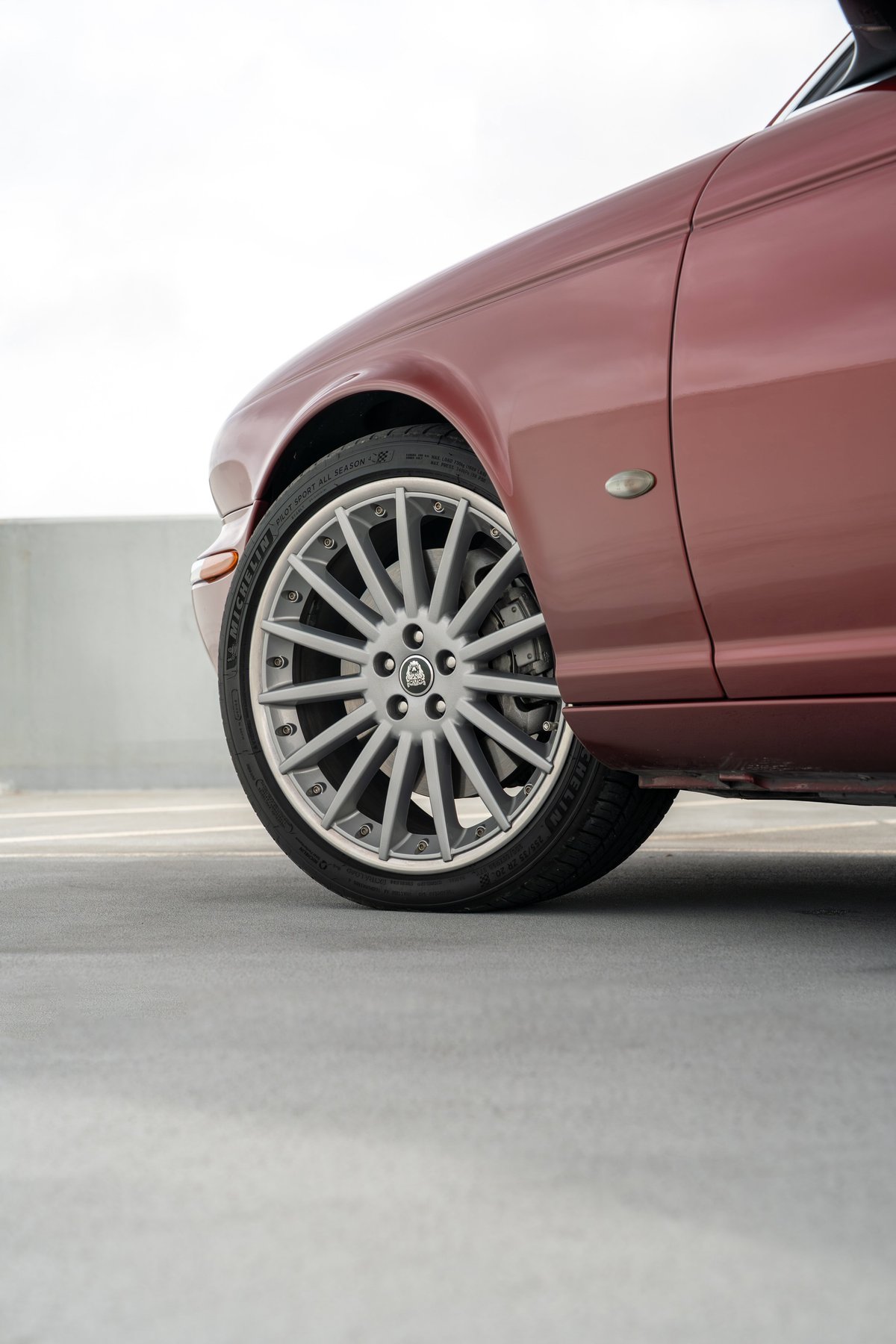 Close-up of a 2006 Jaguar XJR's front wheel, showcasing its multi-spoke alloy rims and radiance red paint.