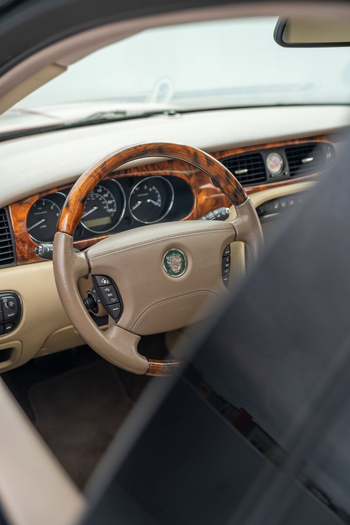 Interior shot of a 2006 Jaguar XJR's steering wheel with wood trim, beige leather, and Jaguar emblem.