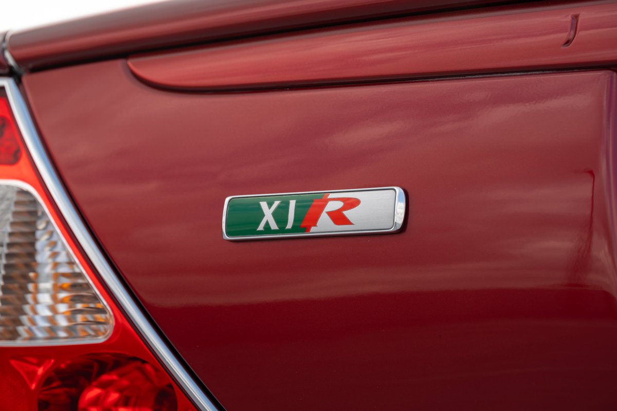 Close-up of a 2006 Jaguar XJR's "XJR" badge in Radiance Red paint.