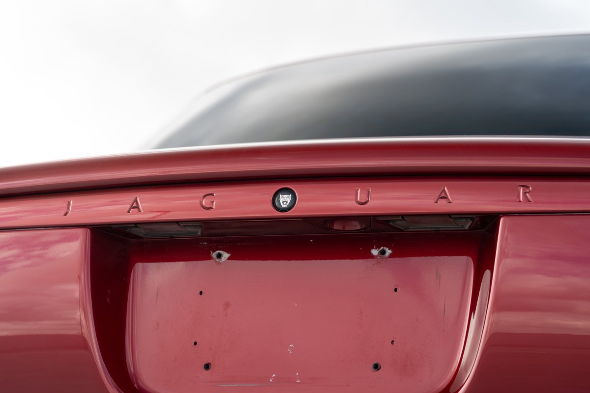 Close up of a red 2006 Jaguar XJR trunk lid with "JAGUAR" badging and license plate mounting holes.