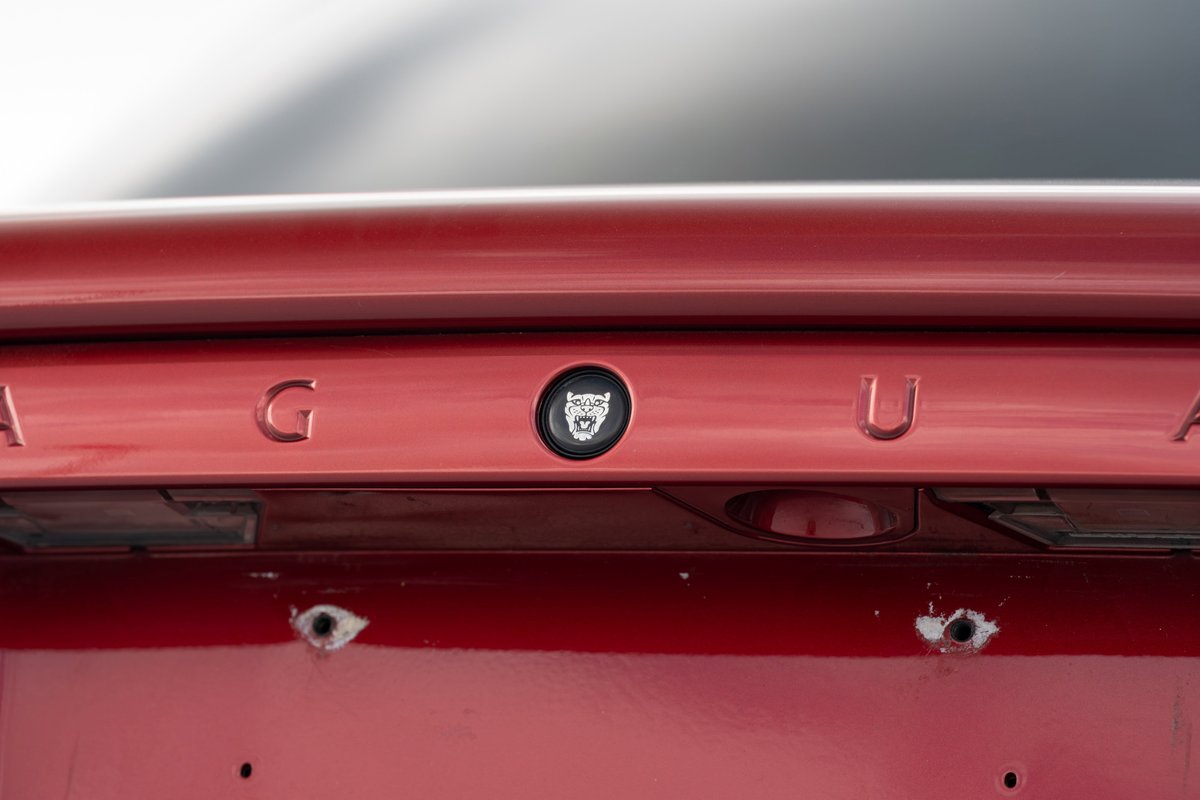 Close-up of red 2006 Jaguar XJR rear trim with chrome lettering and jaguar emblem.