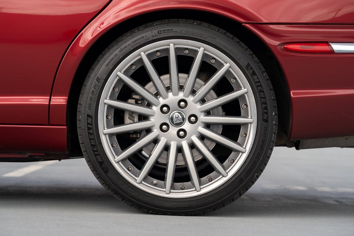 Close up of a red 2006 Jaguar XJR's silver multi-spoke alloy wheel and tire.