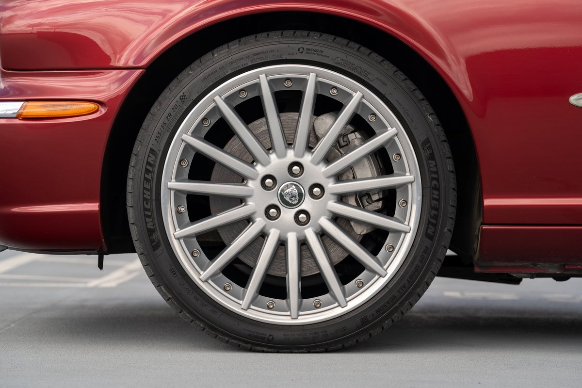 Close-up of a red 2006 Jaguar XJR with silver multi-spoke alloy rims and Michelin tires.