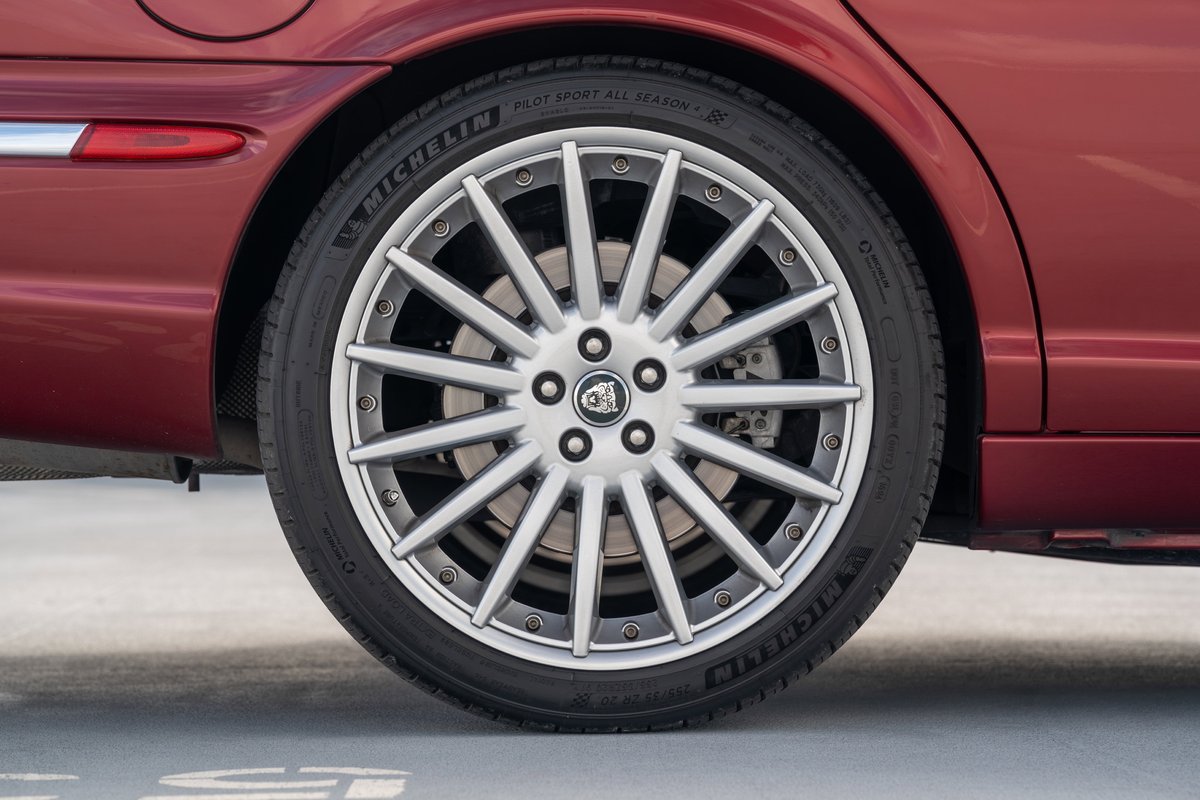 Radiance Red 2006 Jaguar XJR rear wheel with silver multi-spoke rims and Michelin Pilot Sport tires.