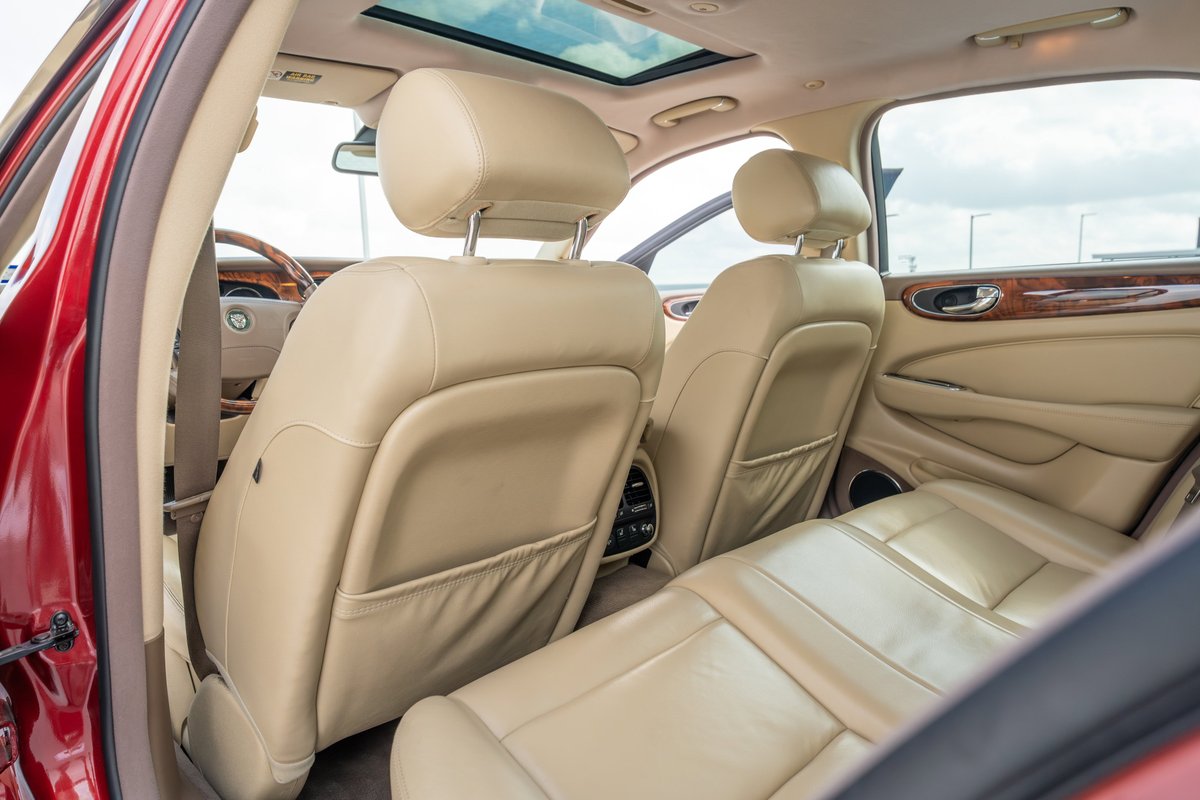 Interior of a 2006 Jaguar XJR in radiance red, featuring beige leather seats, wood trim, and sunroof.