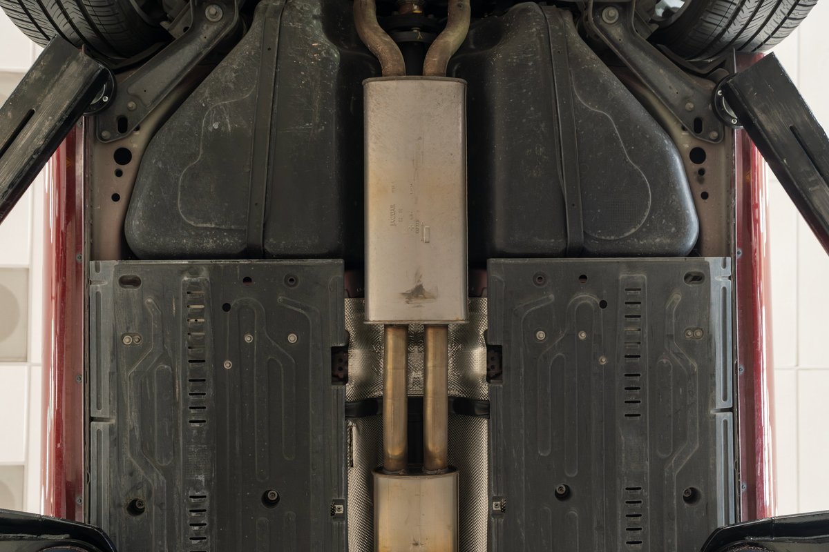 Undercarriage of a 2006 Jaguar XJR in Radiance Red, showing exhaust, underbody panels, and tire.