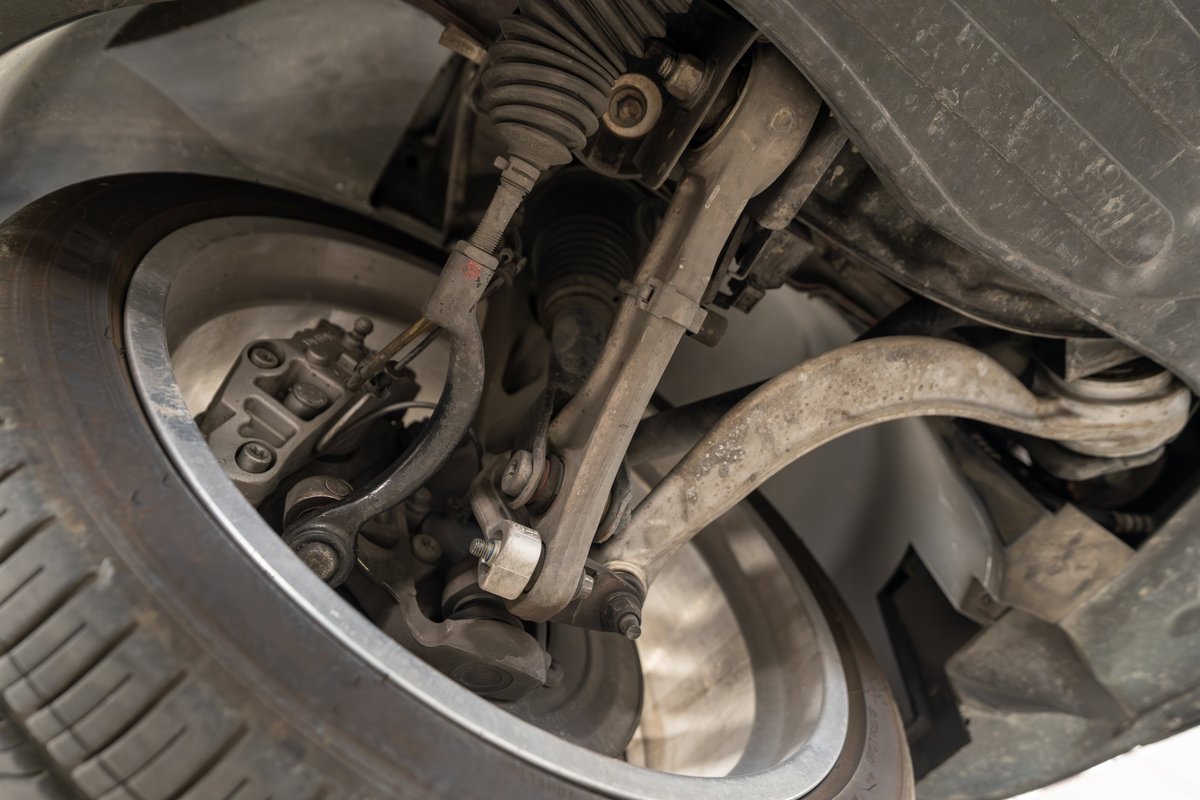 Close-up of 2006 Jaguar XJR's front suspension components, showing aluminum control arms and brake caliper.