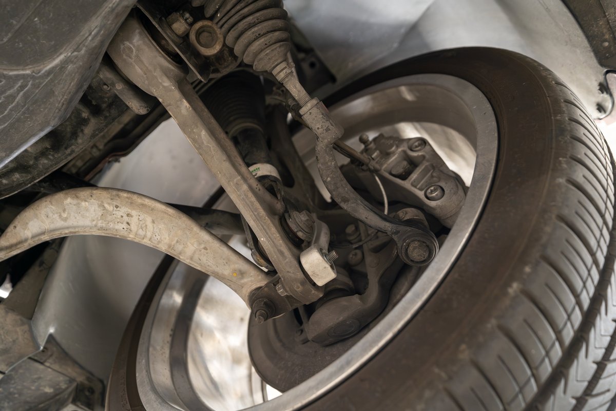 Close-up of the front suspension and wheel of a 2006 Jaguar XJR, showing control arms and brake caliper.