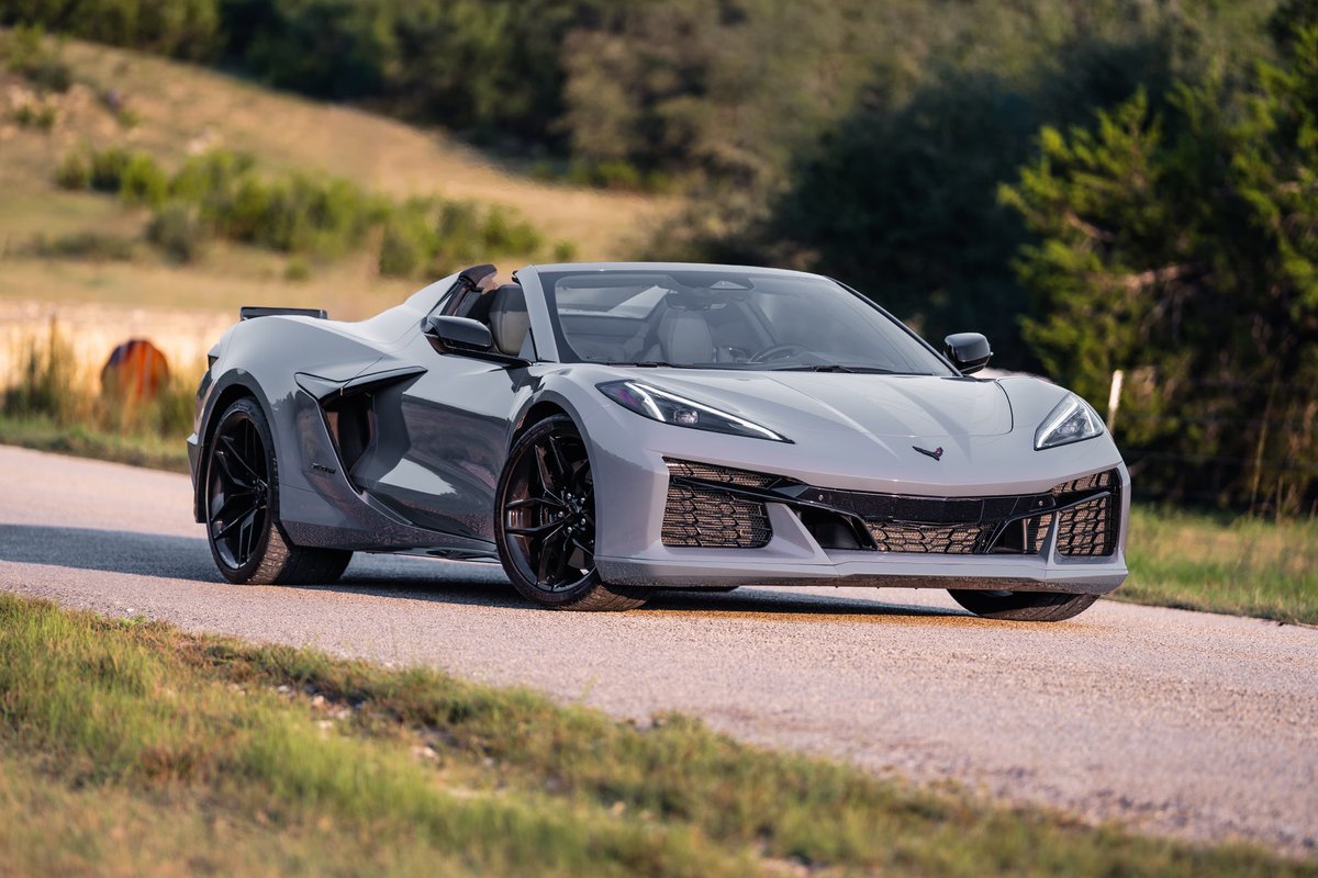 2025 Chevrolet Corvette Z06 convertible in Sea Wolf Gray with black rims and trim, driving on a country road.