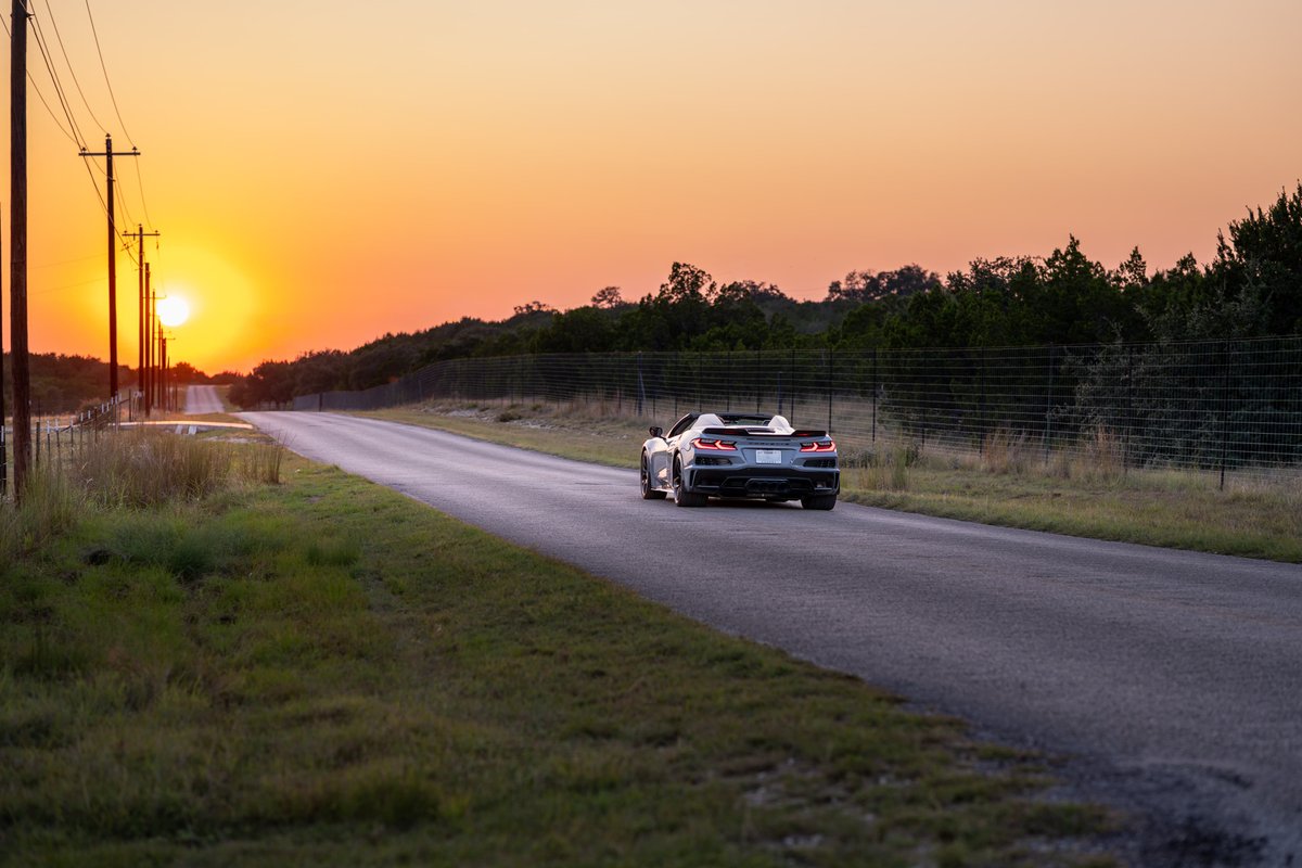 2025 Chevrolet Corvette Z06 convertible in Sea Wolf Gray, driving on a rural road at sunset.